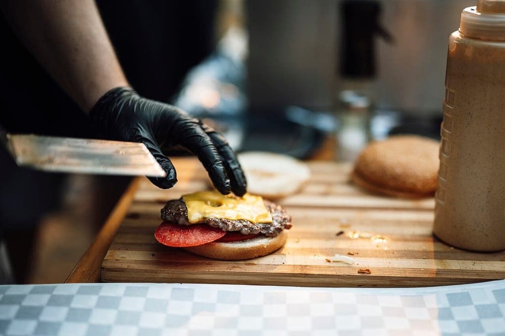 A hamburger being built on a wooden board