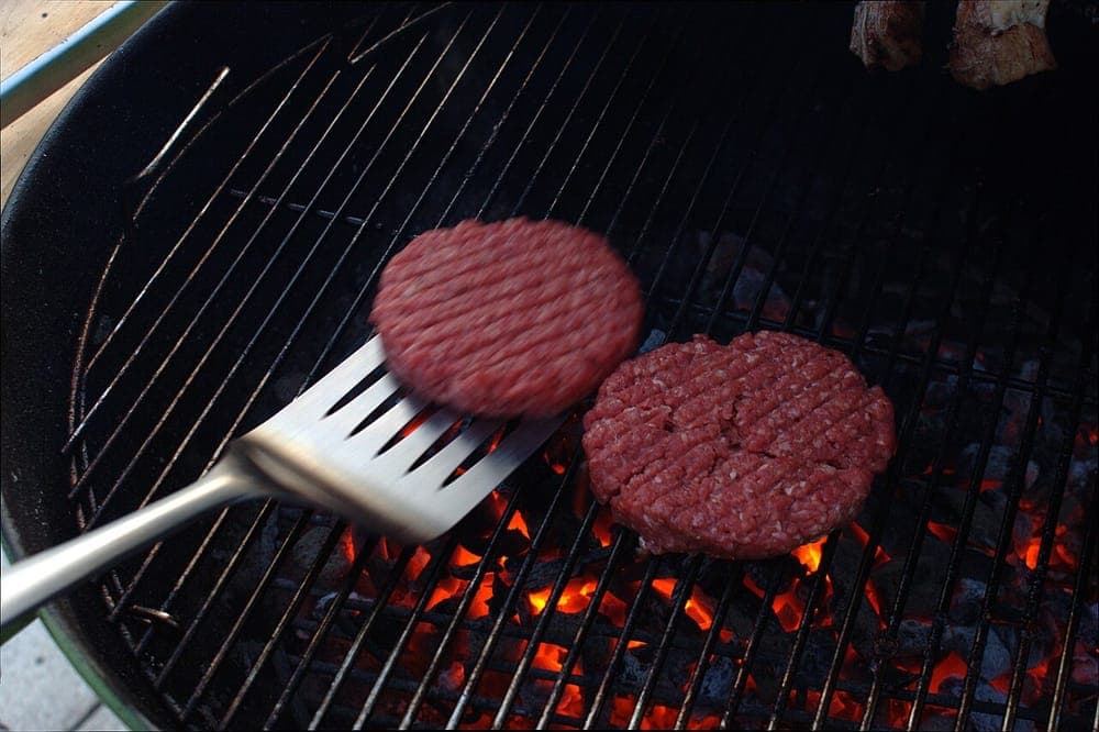 A burger being placed onto a hot cooking surface