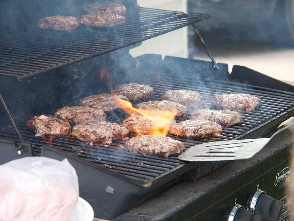 Hamburgers cooking outdoors over propane