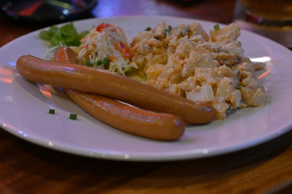 Two grilled sausages plated with potato salad and coleslaw