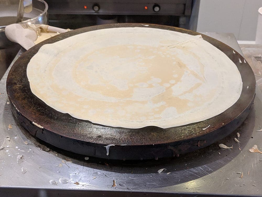 Crepes cooking on a large circular griddle plate